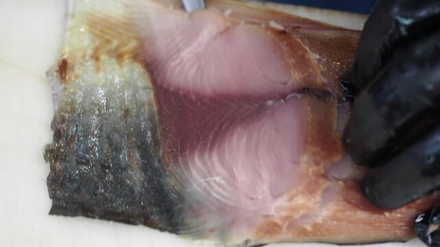 Chef wearing black gloves expertly carves fresh fish fillet, removing bones with precision for a culinary dish