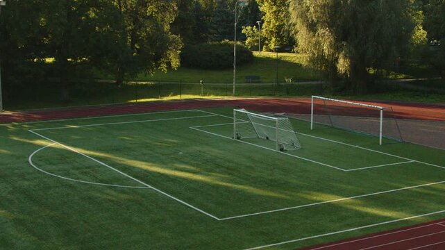 Locked off 4K footage of an empty outdoor football field with full size and portable soccer goals, surrounded by running track and green park in Tallinn, Estonia, illuminated by warm evening sunlight