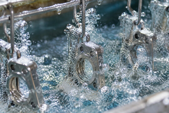 Close-up of metal parts bubbling in an electroplating bath, showing chemical reaction details.