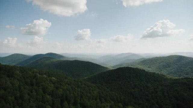 Aerial drone flight over rolling green forested mountains with soft clouds during golden hour