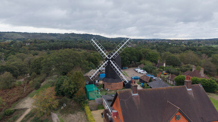 Outwood Windmill, Outwood, Surrey, United Kingdom: Aerial view of the historic 17th-century black smock and post mill with white sails and traditional rural surroundings on a cloudy day. © Serhii
