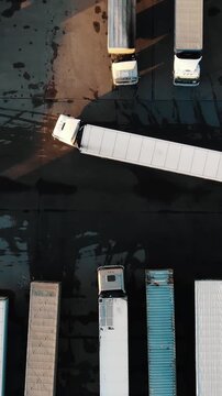 Stunning top down aerial shot captures a large white semi trailer truck expertly reversing into a tight parking spot among other vehicles at a bustling logistics center during sunset
