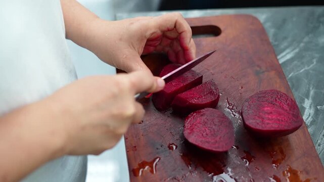 Close-up of hands dicing fresh red beetroot on a wooden cutting board