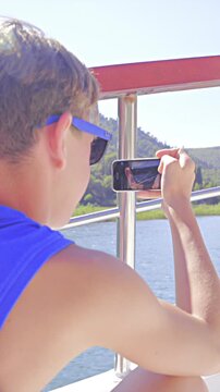 Boy on boat deck filming while sailing on river