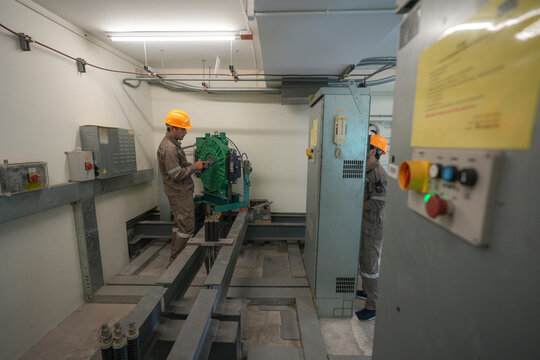 Industrial technician maintenance machinery electrical panel control room, workers in hardhat and coverall inspecting equipment in industrial facility, safety focused engineering task