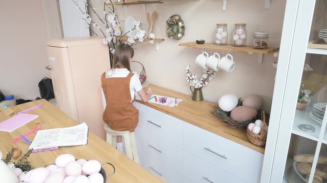 Little girl drawing at kitchen counter decorated with Easter eggs and spring decor