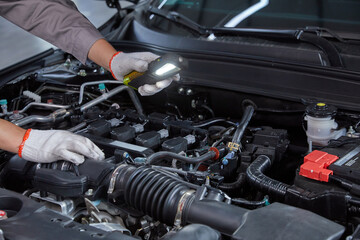 Fototapeta premium Mechanic Inspecting Car Engine with Handheld Light in Auto Repair Workshop