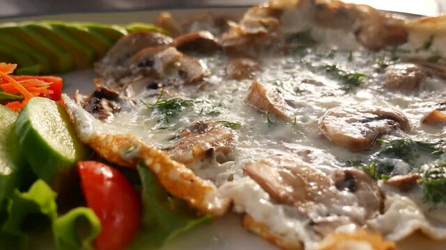 Close up view of fresh mushroom omelette served with cucumbers tomatoes and avocado on white plate