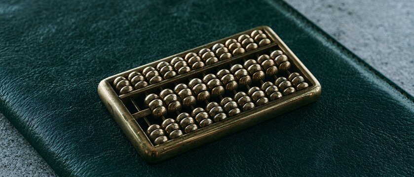 Antique brass abacus resting on a dark green leather blotter with cinematic ambient daylight