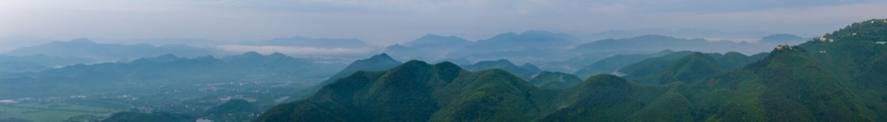 Fototapeta premium Panoramic misty green mountain landscape with layered ridges