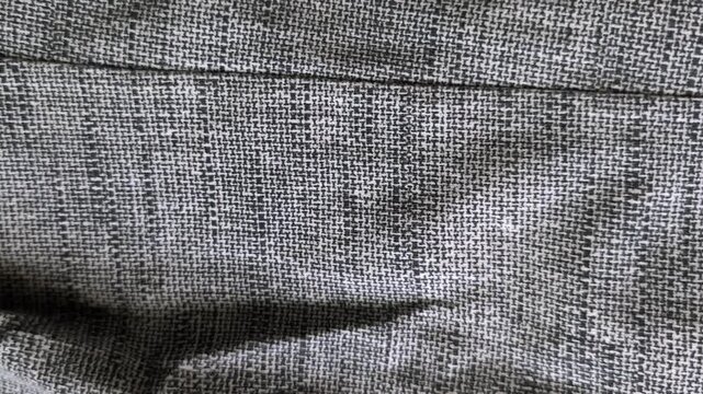 Macro close up of gray plaid fabric texture with detailed woven yarn pattern and horizontal seam, moving subtly to showcase quality suit textile material for elegant fashion background video.