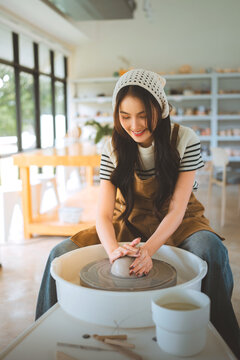 Young woman shaping clay on pottery wheel in bright ceramic studio, creating handmade pottery with traditional craftsmanship, creative skill, artistic hobby.