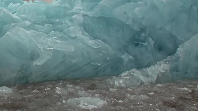 A large blue iceberg fills a close view above dark cold water. Secondary visible features include irregular ice texture, with natural contrast and texture defining the frame.
