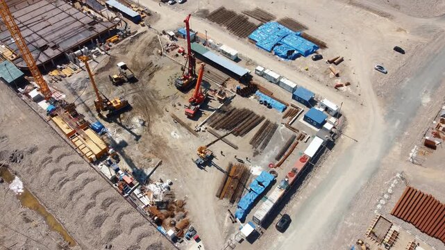 High aerial view showing a piling rig drilling into the ground to create deep foundations for a new building, surrounded by construction machinery, materials, and temporary site offices