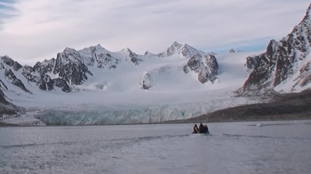 Snowy mountain slopes rise above calm cold coastal water. The surrounding view shows a bay and wide framing, adding visual depth and surface detail to the composition.