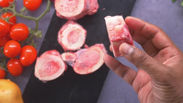 Close-up cinematic motion of hand holding raw beef bone with marrow, ready for cooking and preparing nutritious broth