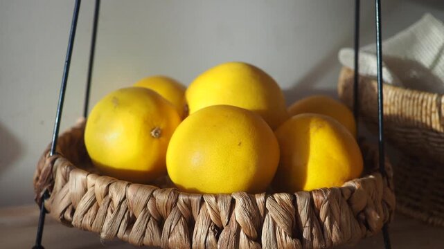 Fresh yellow pomelo fruits in woven basket under soft morning sunlight creating artistic shadows on white wall
