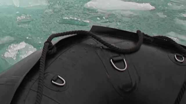 An inflatable boat bow frames cold water surrounded by floating ice. The scene also contains close framing, with the framing revealing natural texture and spatial depth.