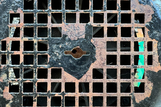 old rusty cast iron grate with square holes pattern