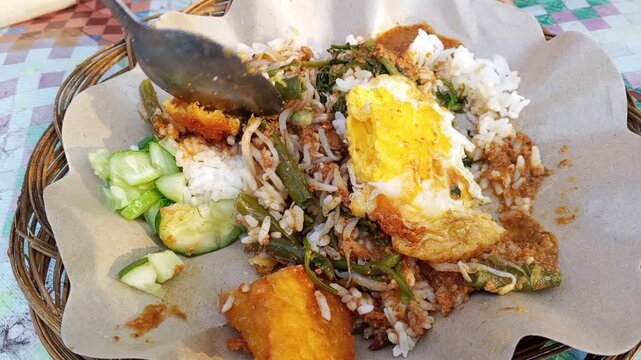 Eating traditional Indonesian nasi pecel with peanut sauce and fried egg

