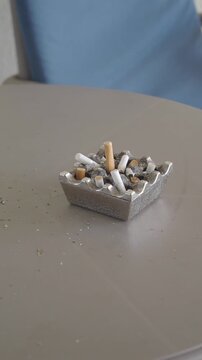 Full metal ashtray with cigarette butts on outdoor table at daylight