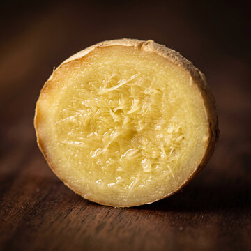 Fresh ginger root cross section slice showing fibrous juicy texture on dark wood surface, macro close-up
