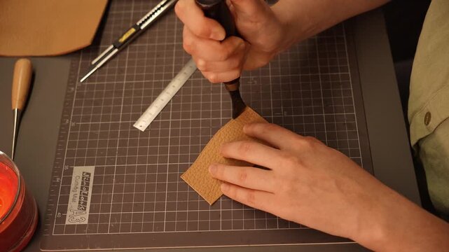 Female artisan thins and shapes the edge of natural leather using a hand skiving tool. Leathercraft process for handmade accessories, fashion, design and small business