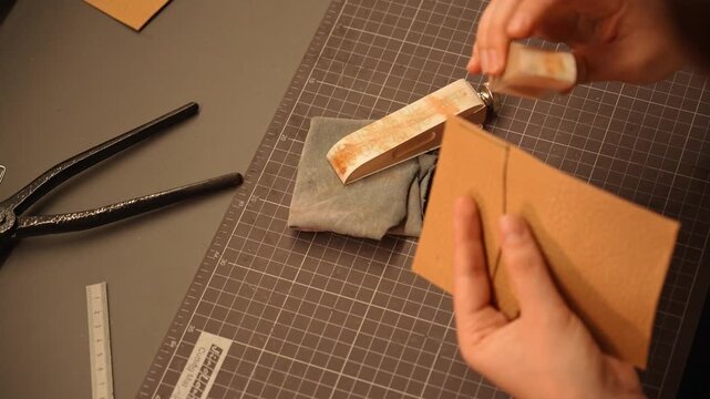 Female artisan sands and smooths the edges of a handmade leather piece with an abrasive block. Leathercraft finishing process for accessories, fashion, design and small business