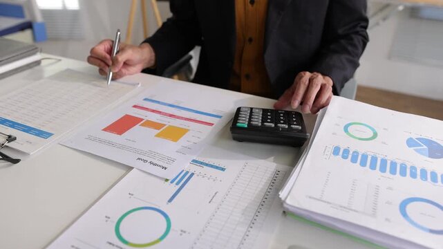 Businessman analyzing financial data using a calculator. Close up of a male accountant or banker reviewing business documents. Office worker checking financial reports, graphs and charts.