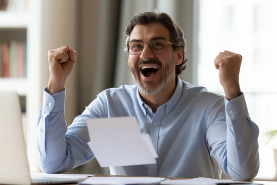 Excited mature businessman celebrating success with fists raised at desk with financial documents
