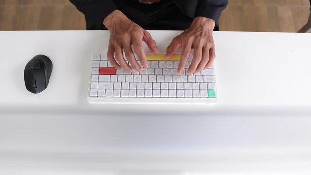 Businessman typing on a modern keyboard at a white office desk. Top view of a professional man's hands typing on a wireless keyboard. Male office worker writing an email on a modern computer.