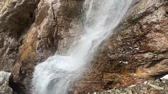 A high-action, close-up view of powerful water spray blasting off a rugged rocky ledge at a mountain waterfall in Khyber Pakhtunkhwa, Pakistan, September