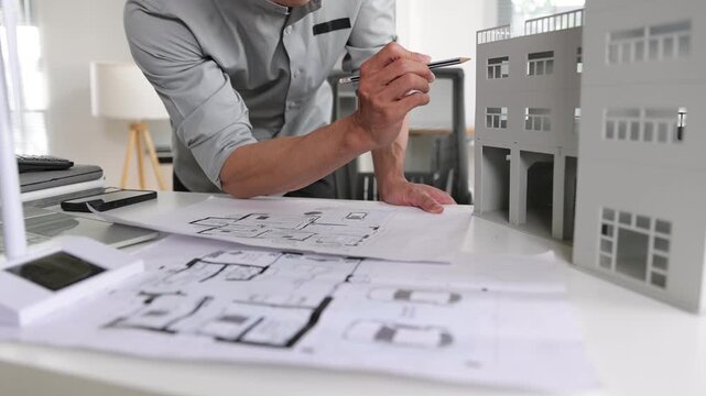 Architect examining blueprints and a building model in the office. Architect pointing at an architectural model and working on building plans in the office. Engineering and real estate development.