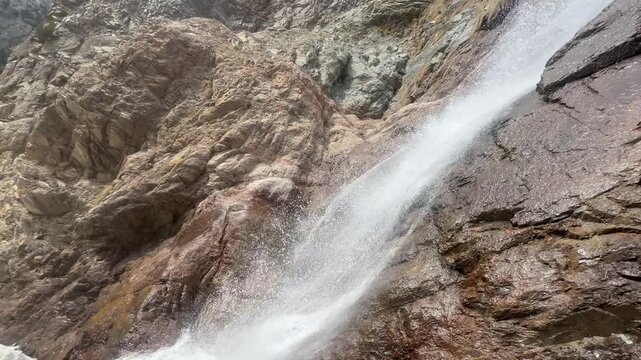 A high-action, close-up view of powerful water spray blasting off a rugged rocky ledge at a mountain waterfall in Khyber Pakhtunkhwa, Pakistan, September