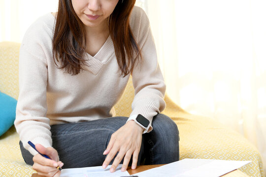 自宅のリビングで書類を書くアジア人の女性