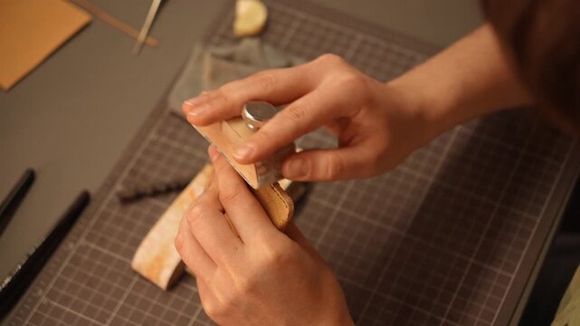 Female artisan sands and smooths the edges of a handmade leather piece with an abrasive block. Leathercraft finishing process for accessories, fashion, design and small business