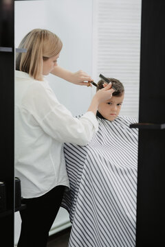 Cute Caucasian boy in a barbershop getting a haircut from a female hairdresser. Stylist's hands with tools. Children's fashion in the salon.