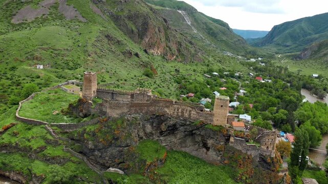 Khertvisi fortress, a medieval stone castle with towers and walls, standing on a high rocky hill in a lush green valley at the confluence of two rivers in southern georgia
