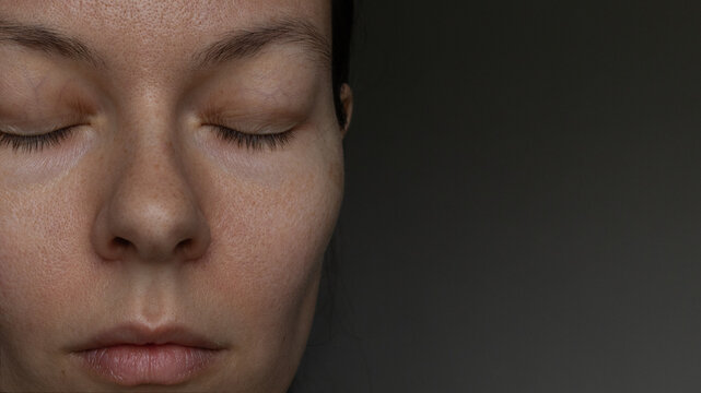 Close-up portrait of a young woman with closed eyes, natural skin texture and freckles.