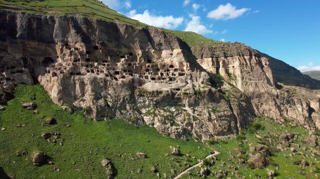 Aerial view moving alongside the ancient cave city of vardzia, a historic monastery complex carved into the erusheti mountain, showcasing its many levels and dwellings under a blue sky