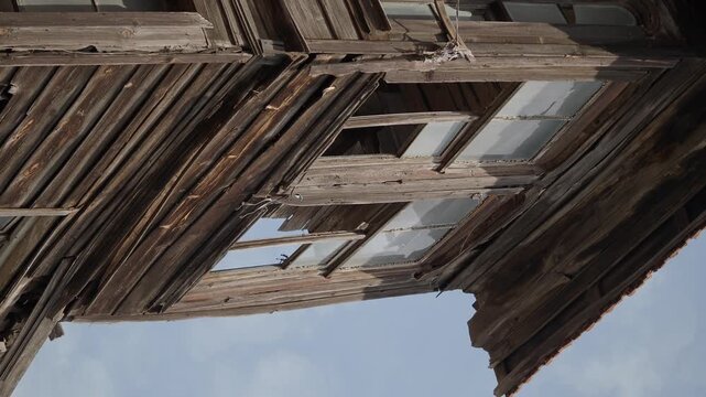 Aged wooden facade with broken windows on old abandoned house under blue sky.