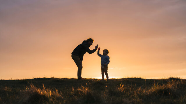 A heartwarming silhouette of a father and son sharing a high-five against a breathtaking sunset, symbolizing their strong bond, joyful connection, and cherished family moments outdoors