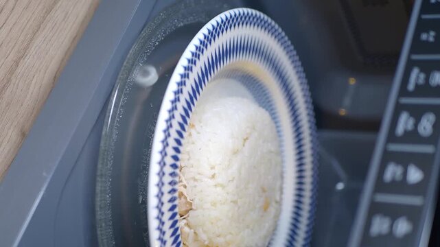 Plate of white rice with chicken pieces rotating inside microwave oven for quick heating up.