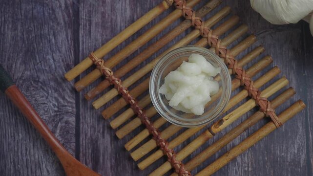 Chopped garlic paste in small bowl on wooden background with spoon and garlic heads.