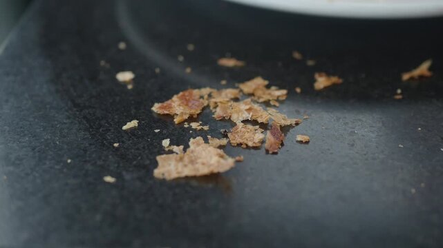 Macro view of scattered brown bread crumbs resting on dark textured kitchen surface indoors.
