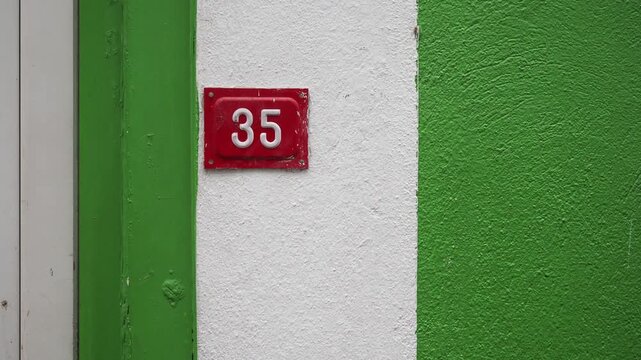 Red house number thirty five on white and green wall section showing urban street details.