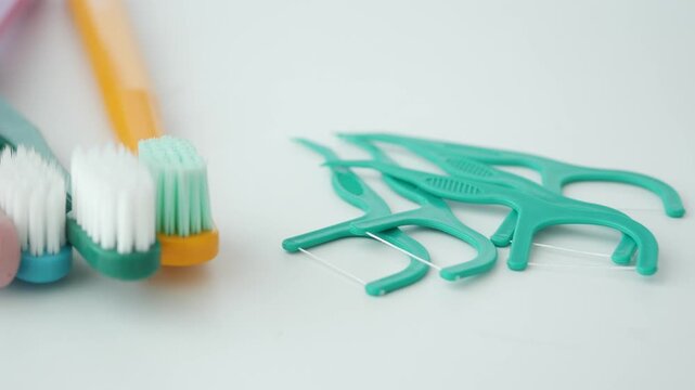 Dental hygiene tools on white surface including colorful toothbrushes and mint floss picks.
