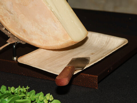 Demi-meule de fromage &agrave; raclette fondant sous un appareil chauffant avec spatule de service