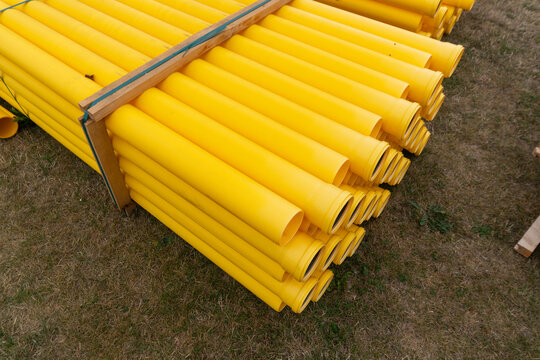 Bright yellow plastic utility pipes are bundled in wooden transport frames and stored on grass before installation. Commercial construction image for underground utility systems, pipeline projects, ci