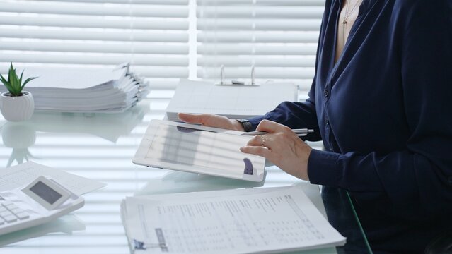 Professional woman using digital tablet for business tasks, typing data and reviewing documents at a modern office desk, symbolizing efficiency and financial management